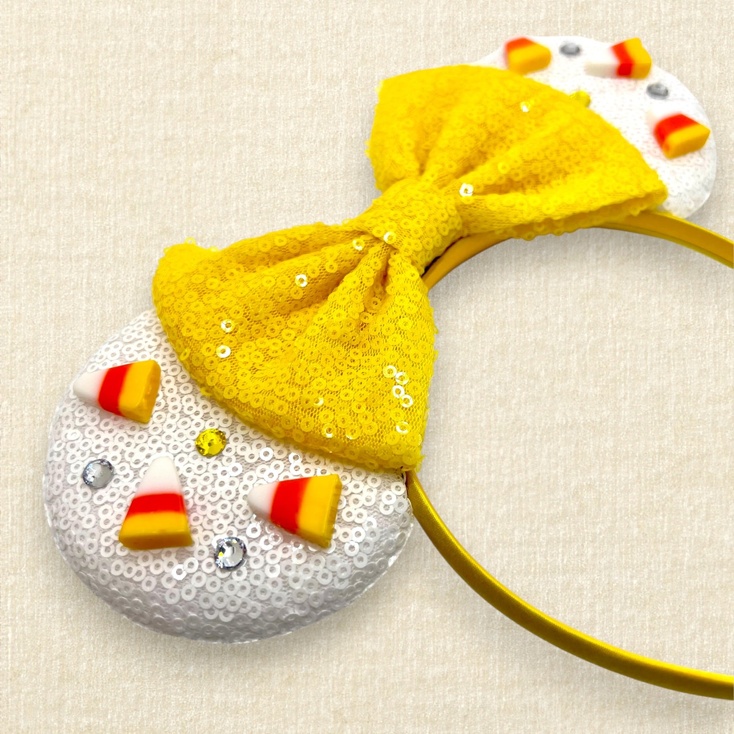 Halloween-themed mouse ears headband with white ears, candy corn pieces, rhinestones, and a yellow bow