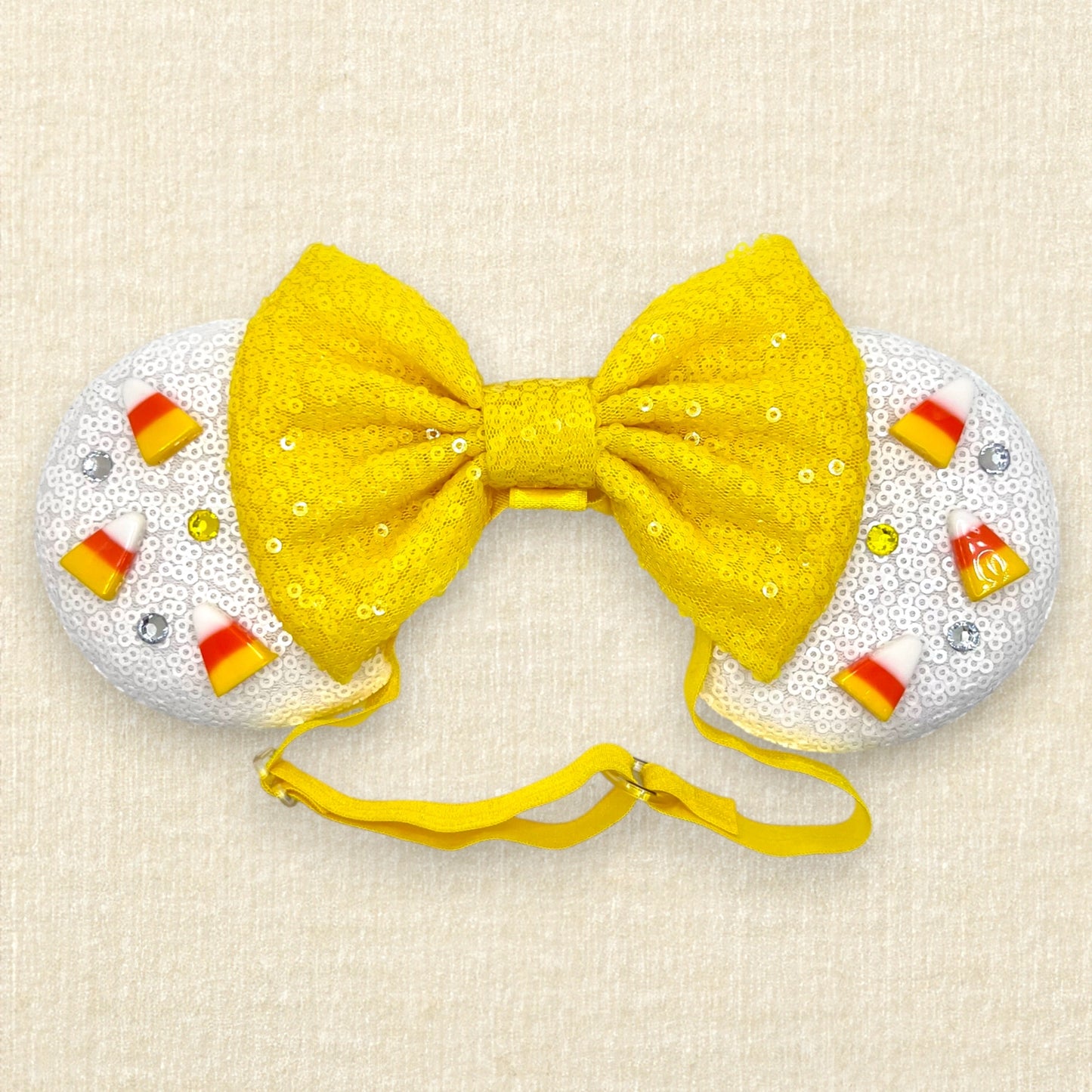 Halloween-themed mouse ears with white sequin ears, candy corn pieces, rhinestones, and yellow sequin bow on an elastic headband