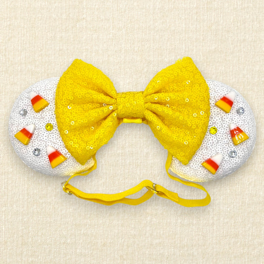 Halloween-themed mouse ears with white sequin ears, candy corn pieces, rhinestones, and yellow sequin bow on an elastic headband