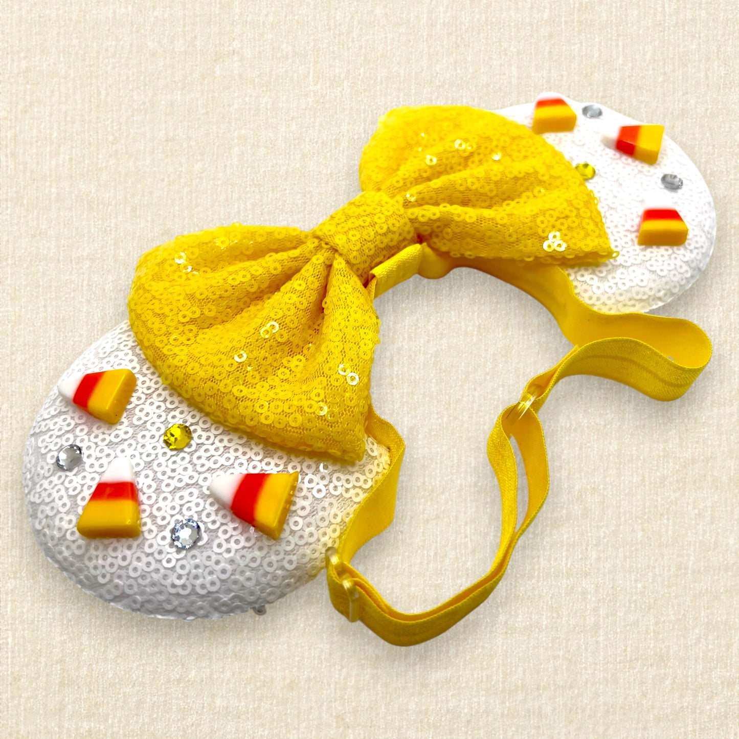 Halloween-themed mouse ears with white sequin ears, candy corn pieces, rhinestones, and yellow sequin bow on an elastic headband
