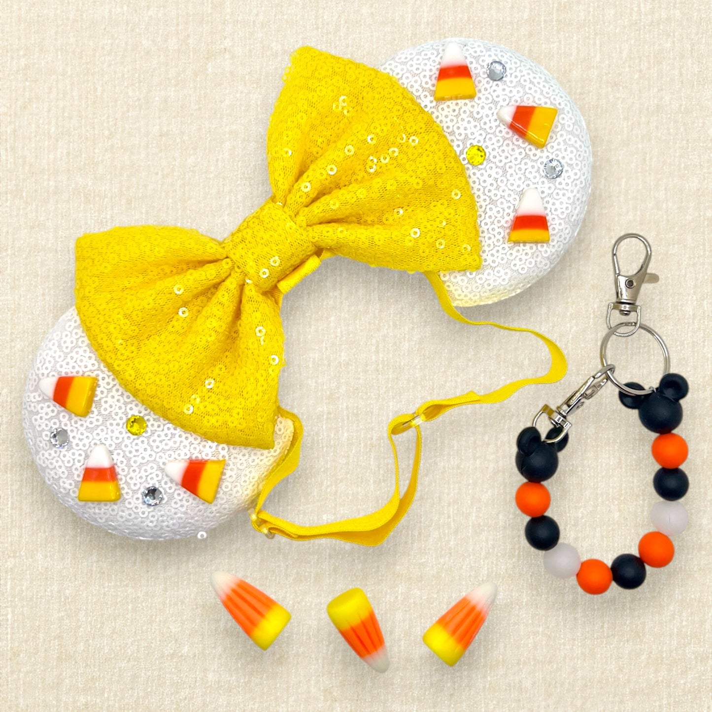 Halloween-themed mouse ears with white sequin ears, candy corn pieces, rhinestones, and yellow sequin bow on an elastic headband; candy corn pieces; black and orange beaded mouse ears holder keychain
