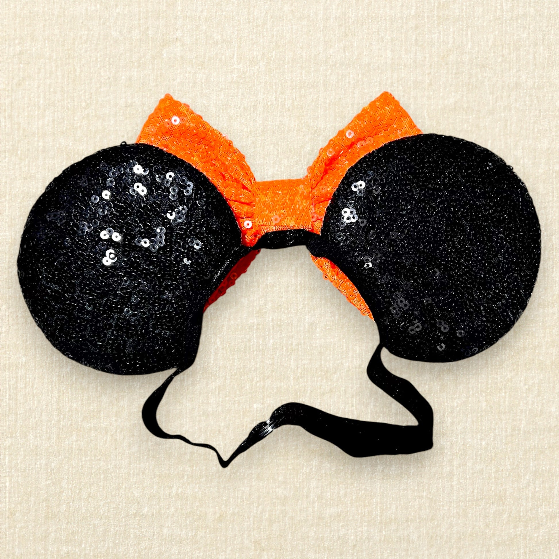 Black sequin Halloween-themed mouse ears with candy corn pieces, rhinestones, and an orange bow on an elastic headband (back view)
