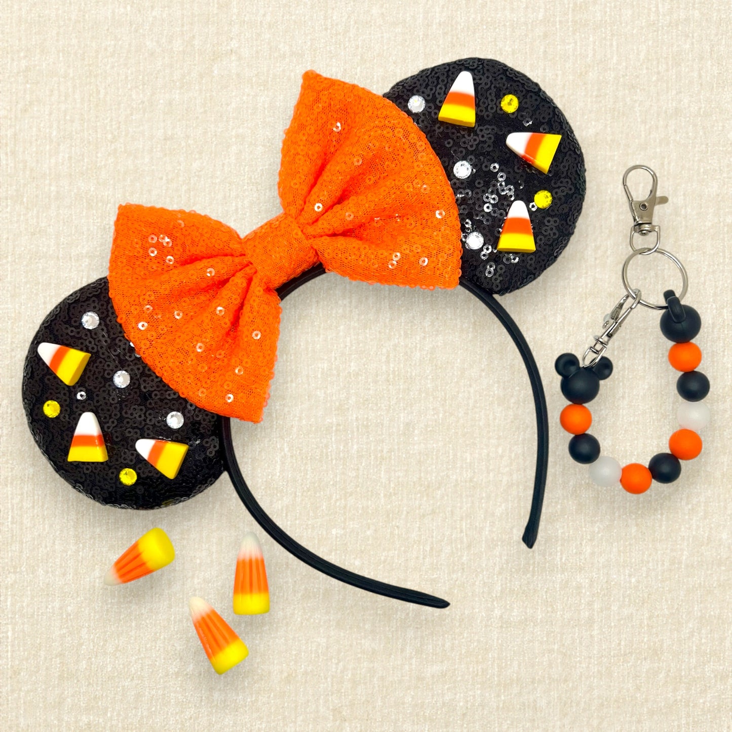 Black sequin Halloween-themed mouse ears with candy corn pieces, rhinestones, and orange sequin bow; decorative candy corn; black and orange beaded mouse ears holder keychain