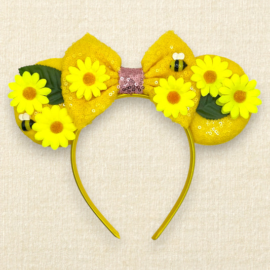 Yellow floral mouse ears headband with yellow daisies and bees and a bow on a beige background