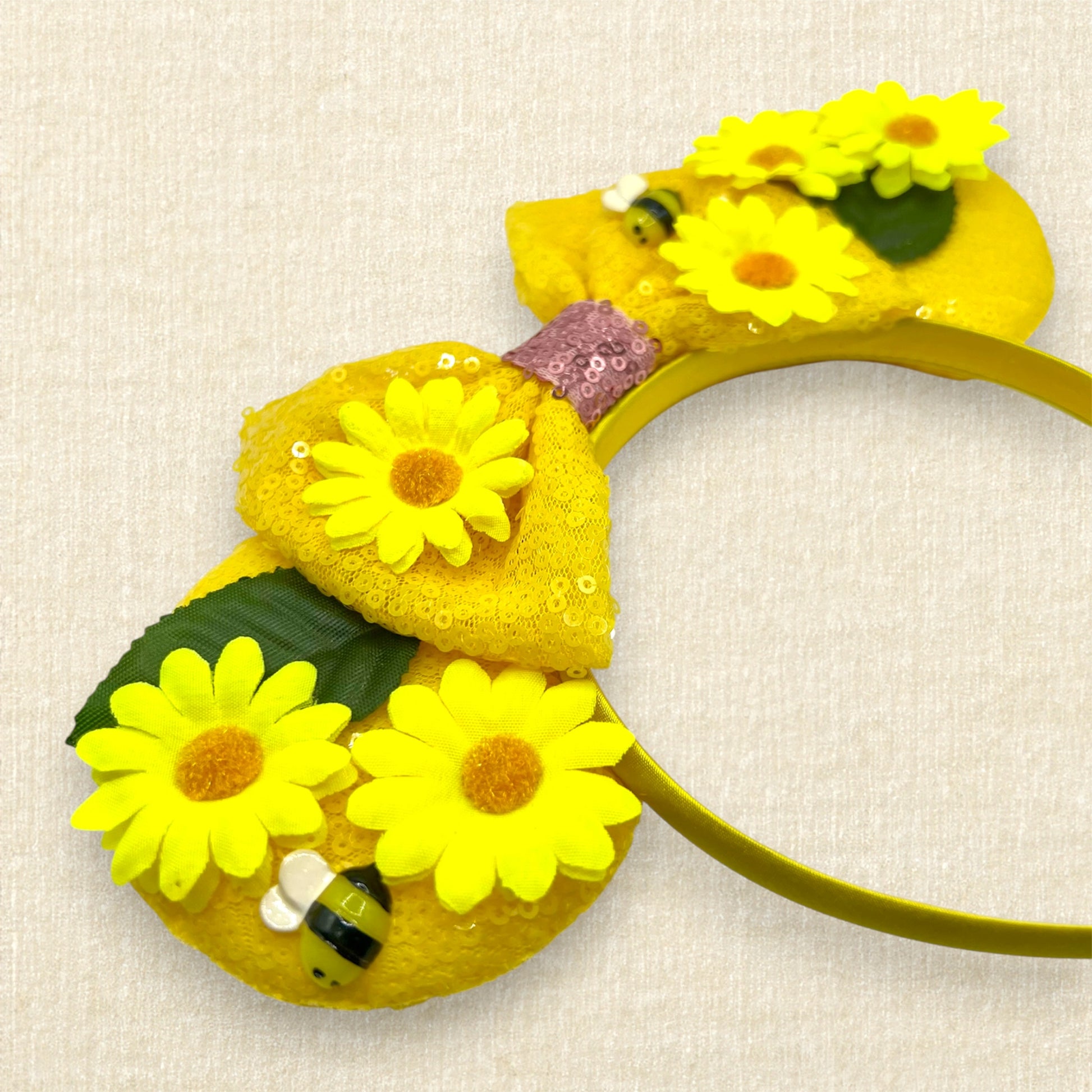 Yellow floral mouse ears headband with yellow daisies and bees and a bow on a beige background