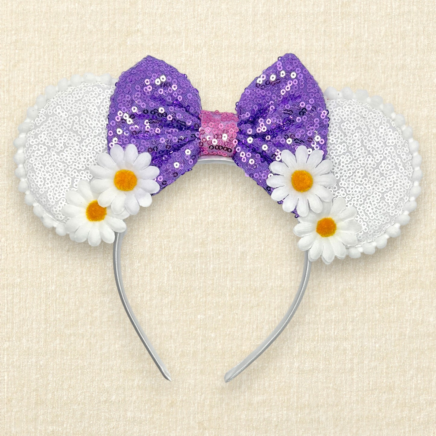 Mouse ears headband with purple sequin bow and white flowers on a beige background