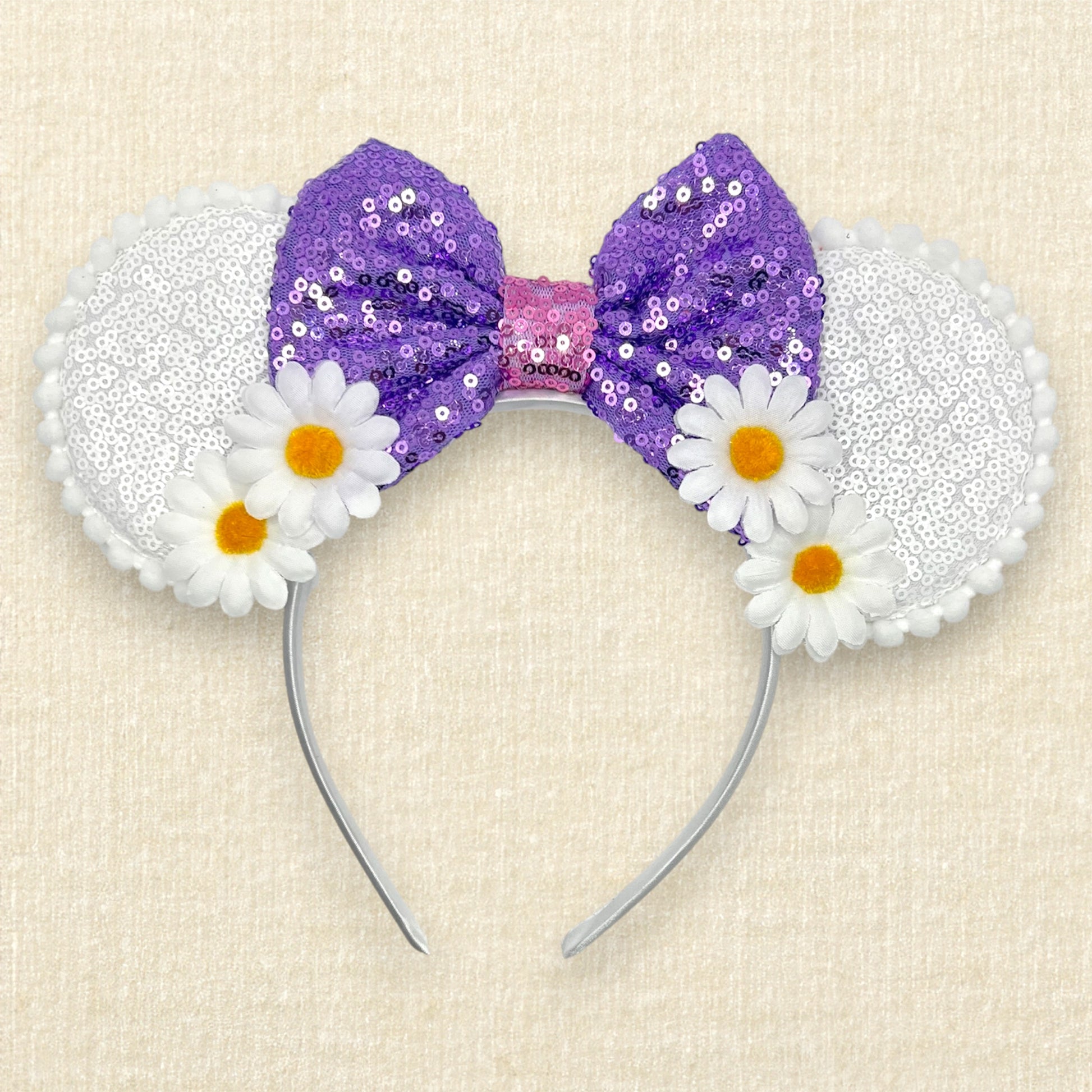 Mouse ears headband with purple sequin bow and white flowers on a beige background