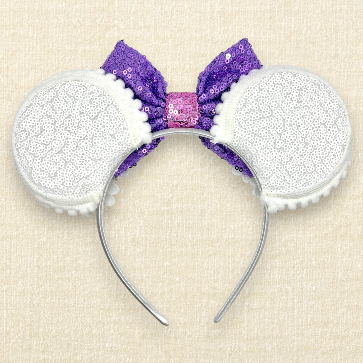 Mouse ears headband with purple sequin bow and white flowers on a beige background (back view)