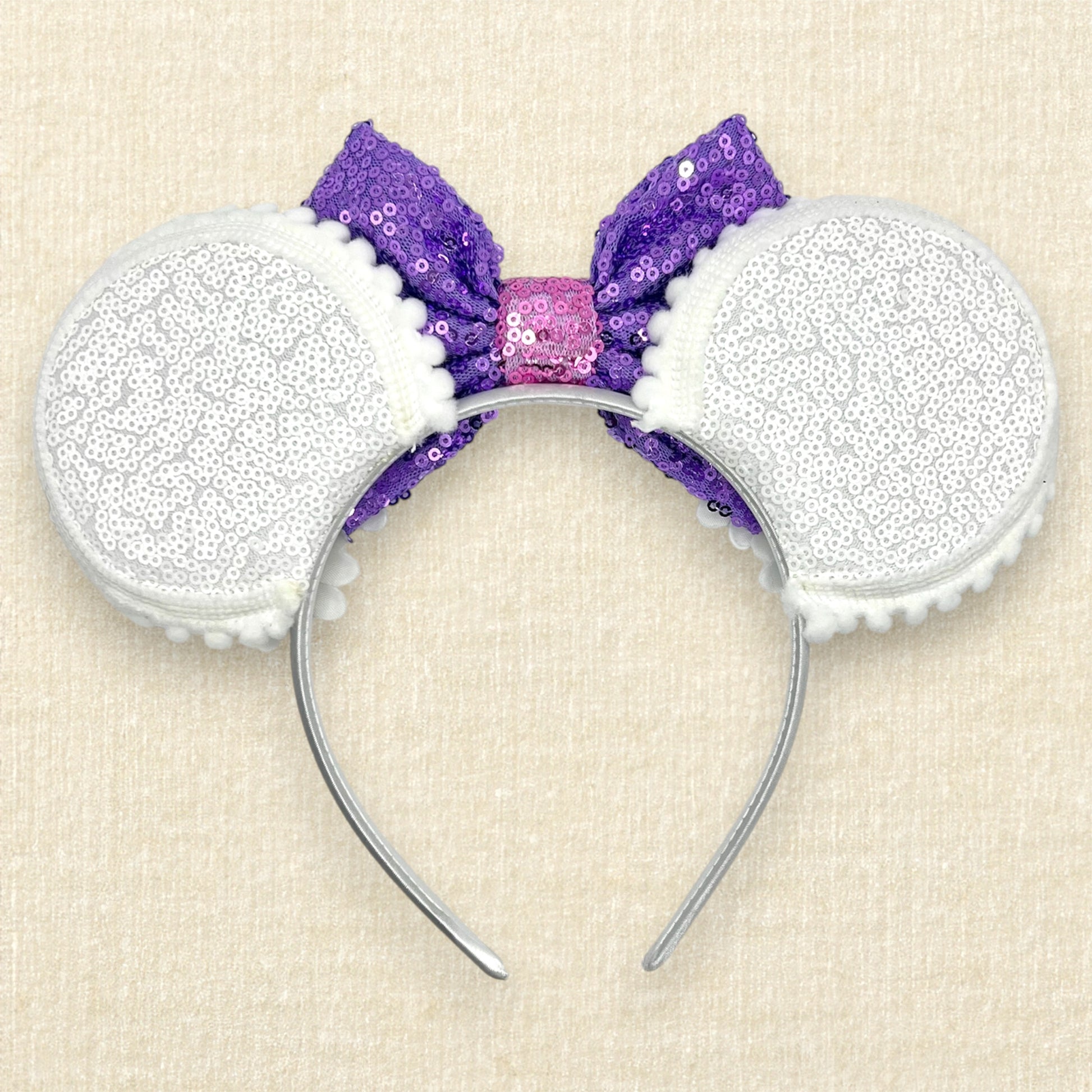 Mouse ears headband with purple sequin bow and white flowers on a beige background (back view)