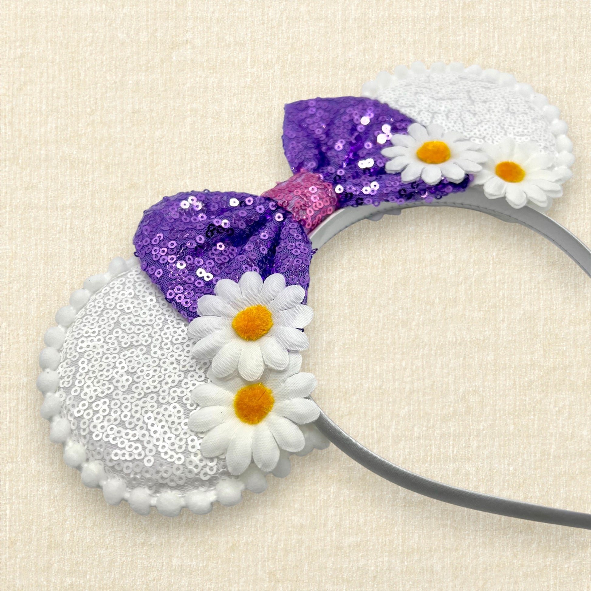Mouse ears headband with purple sequin bow and white flowers on a beige background