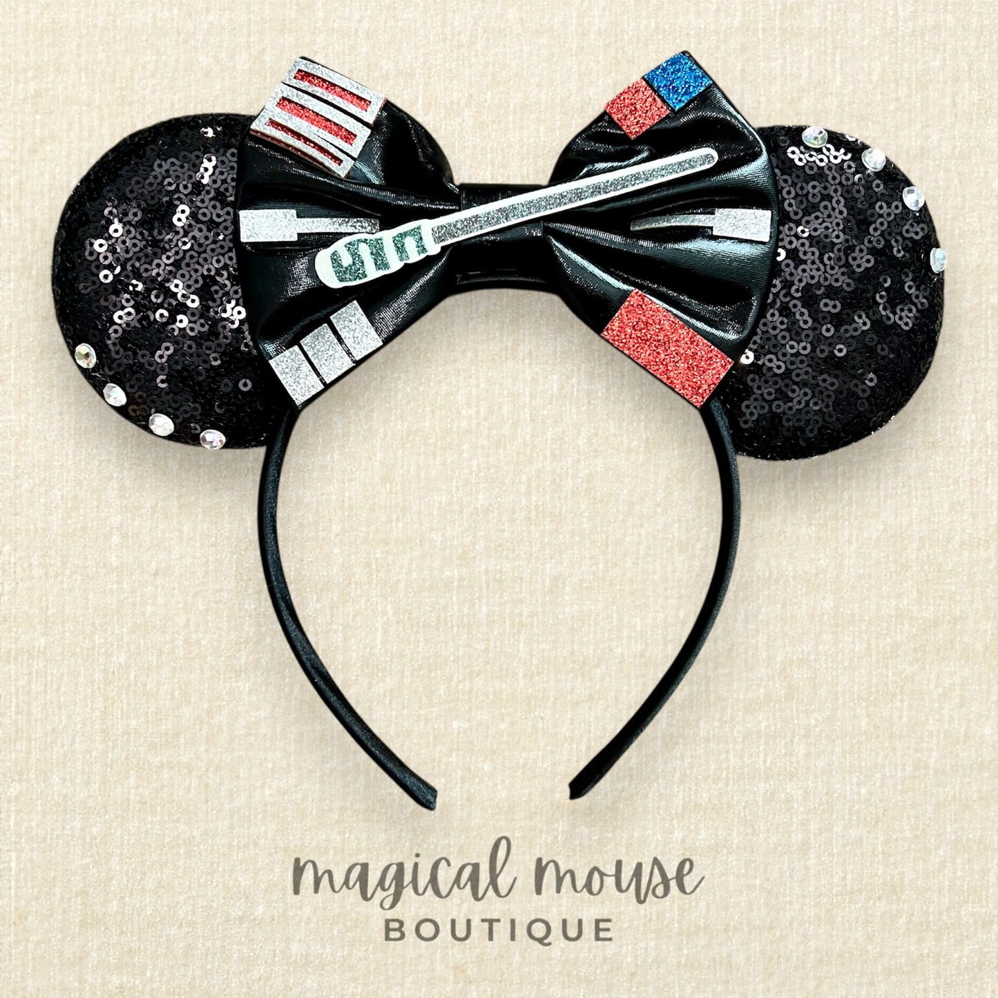 Black Minnie Mouse ears with a bow and red, silver, and blue accents on a beige background, branded 'magical mouse Boutique'.