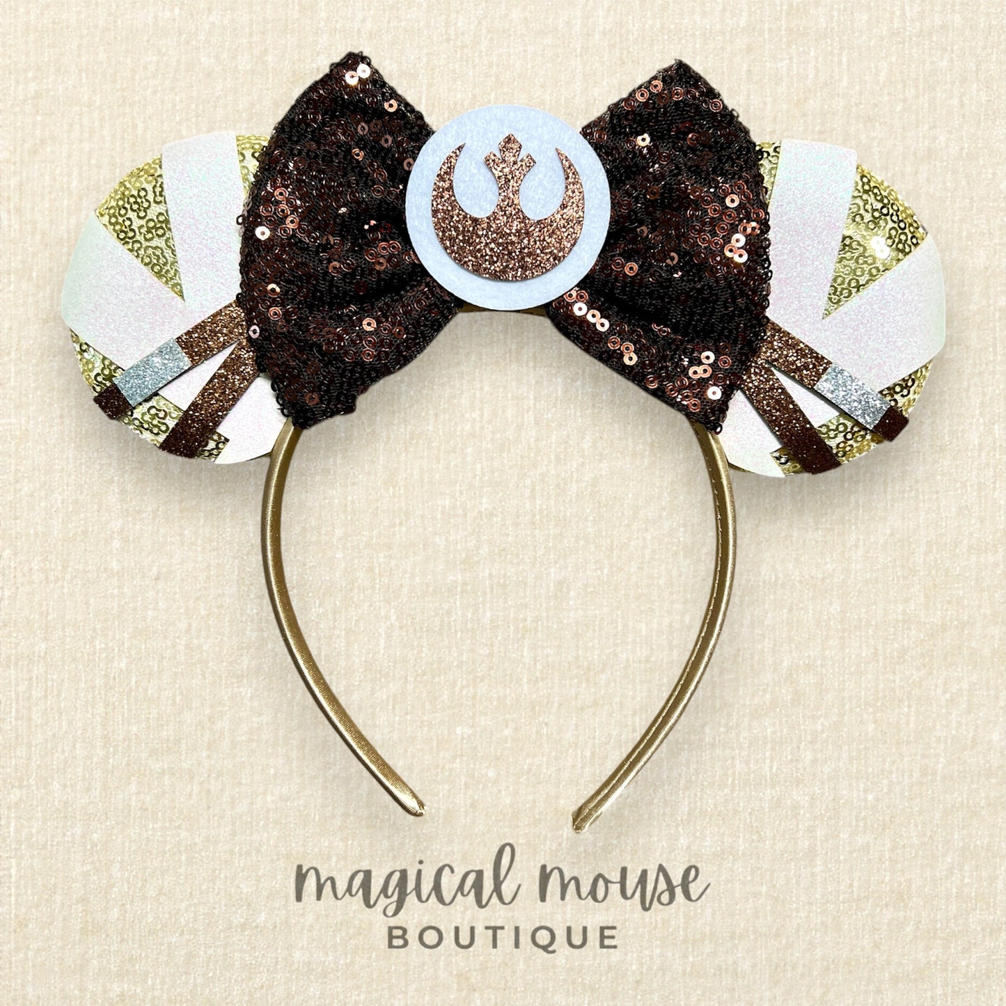 Decorative headband with a bow and emblem on a beige background, branded 'Magical Mouse Boutique'.