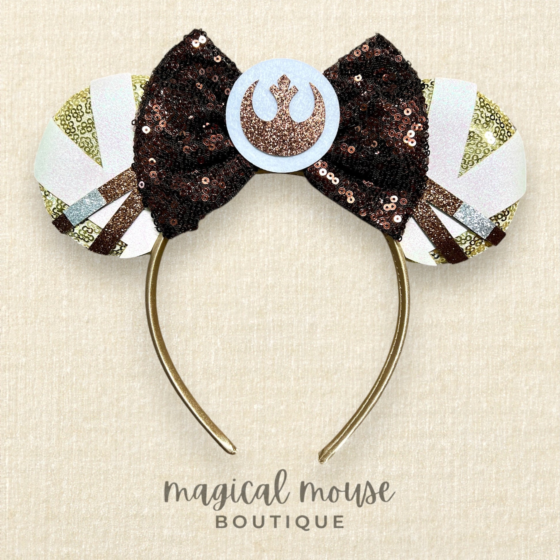 Decorative headband with a bow and emblem on a beige background, branded 'Magical Mouse Boutique'.