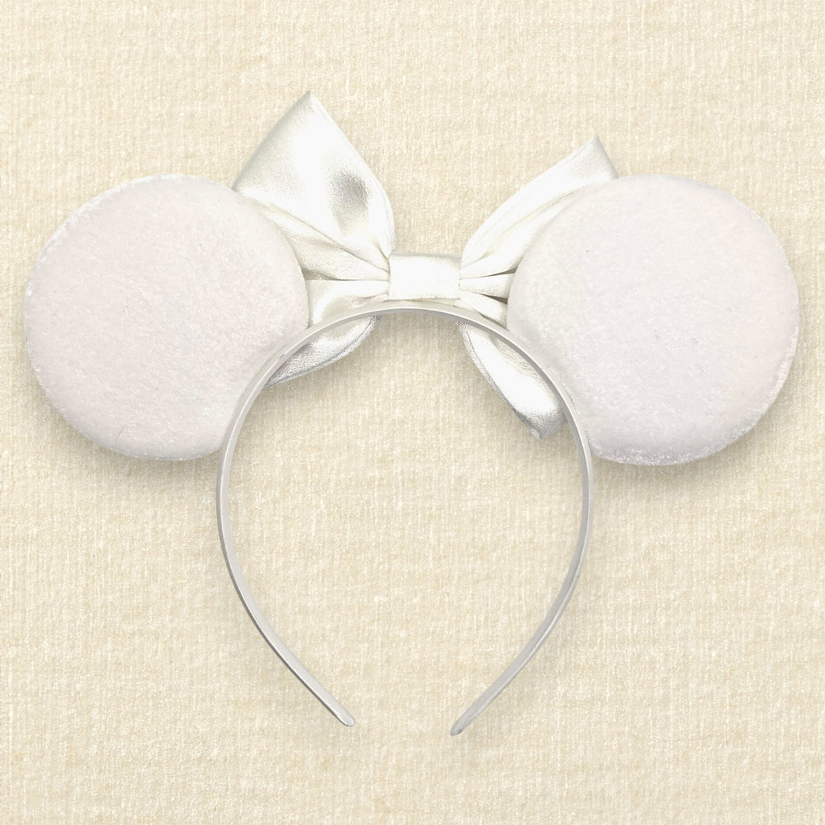 Winter-themed white velvet mouse ears headband with a large white satin bow and decorative blue and silver rhinestones on a textured beige background (back view)