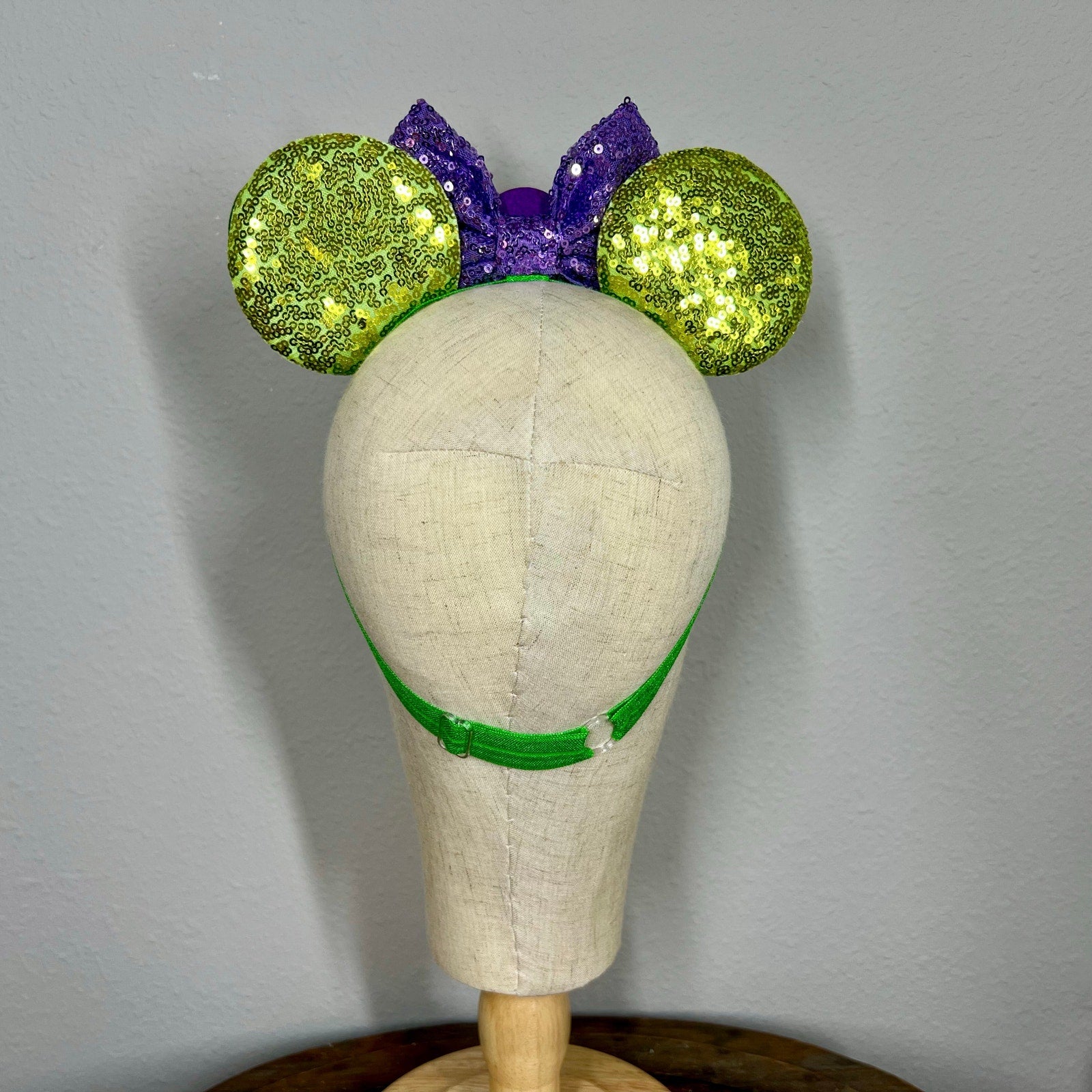 Green and purple headband with glittery ears on a mannequin head against a gray background
