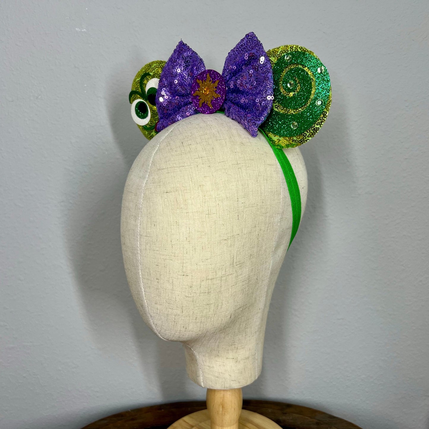Decorative mouse ears headband with purple and green elements on a mannequin head against a gray background