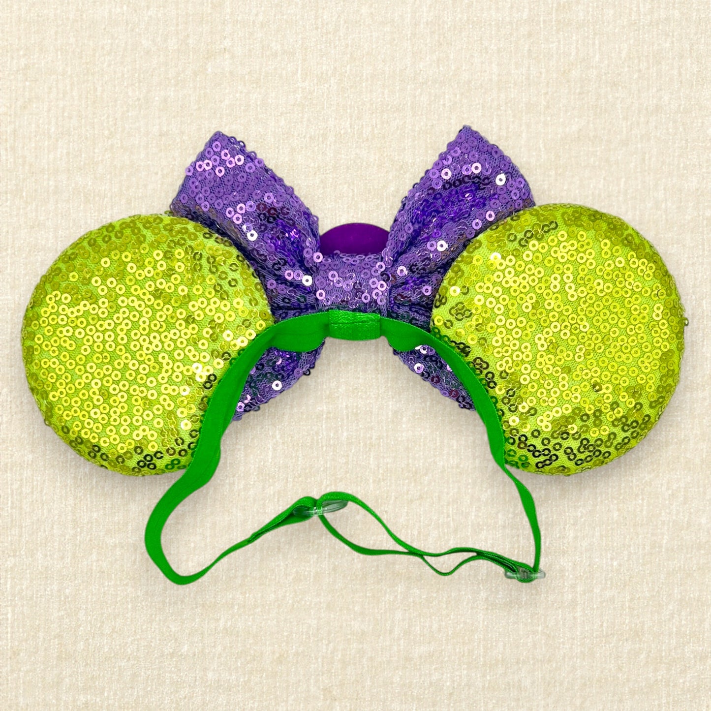 Green sequin mouse ears with glitter chameleon details, purple sequin bow with yellow sun centerpiece, and rhinestones on an elastic headband (back view)
