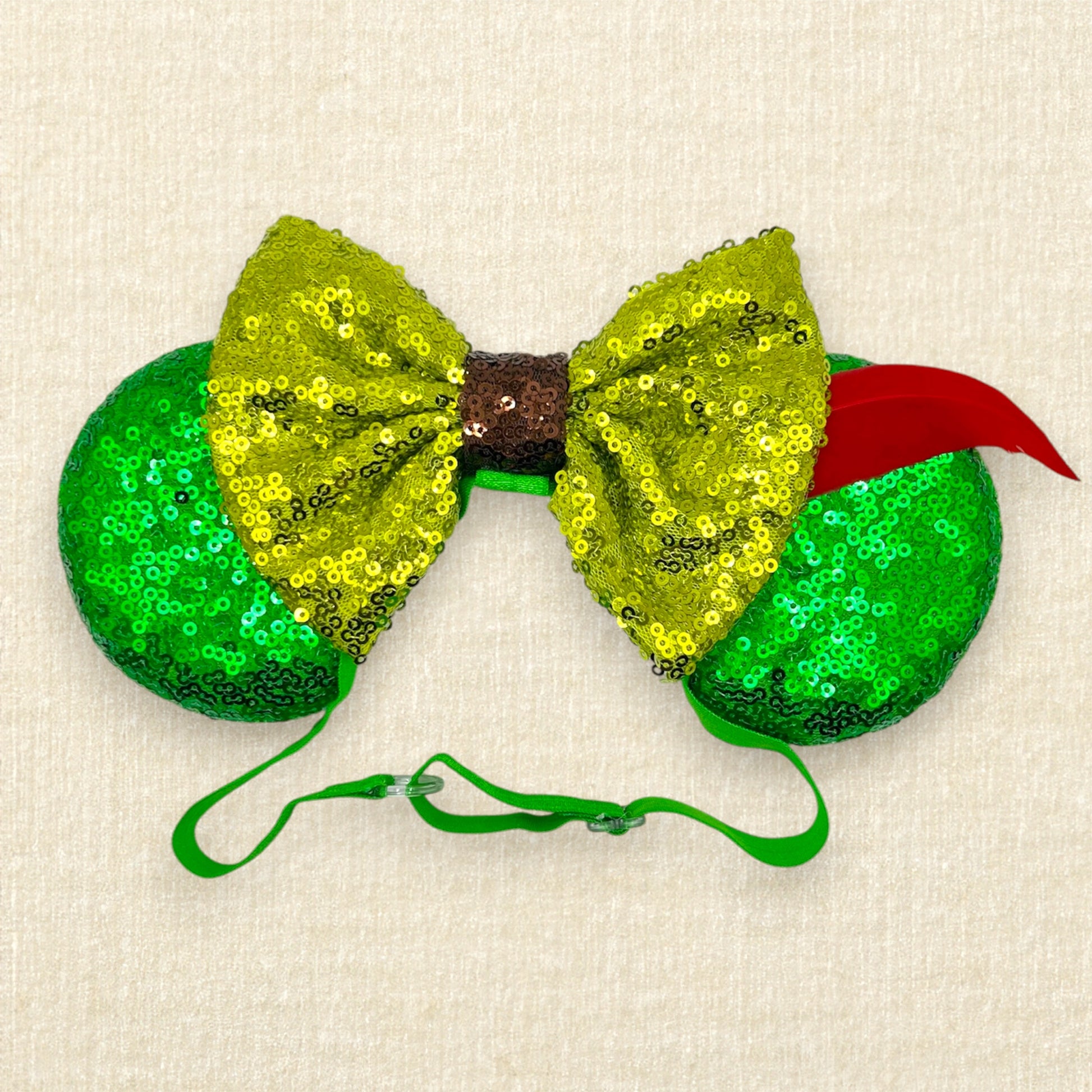 Green sequin mouse ears with lighter green sequin bow and red feather on an elastic headband