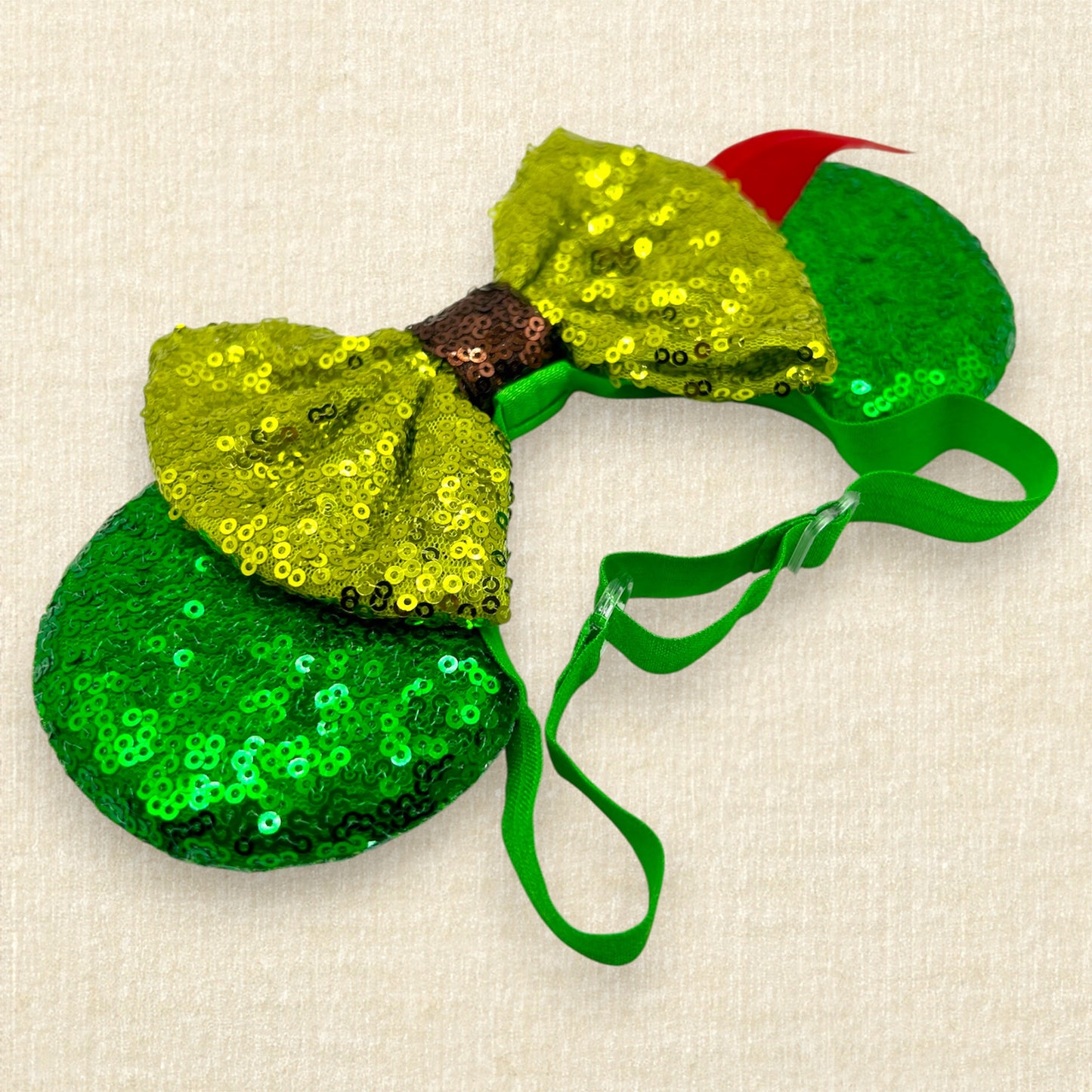 Green sequin mouse ears with lighter green sequin bow and red feather on an elastic headband