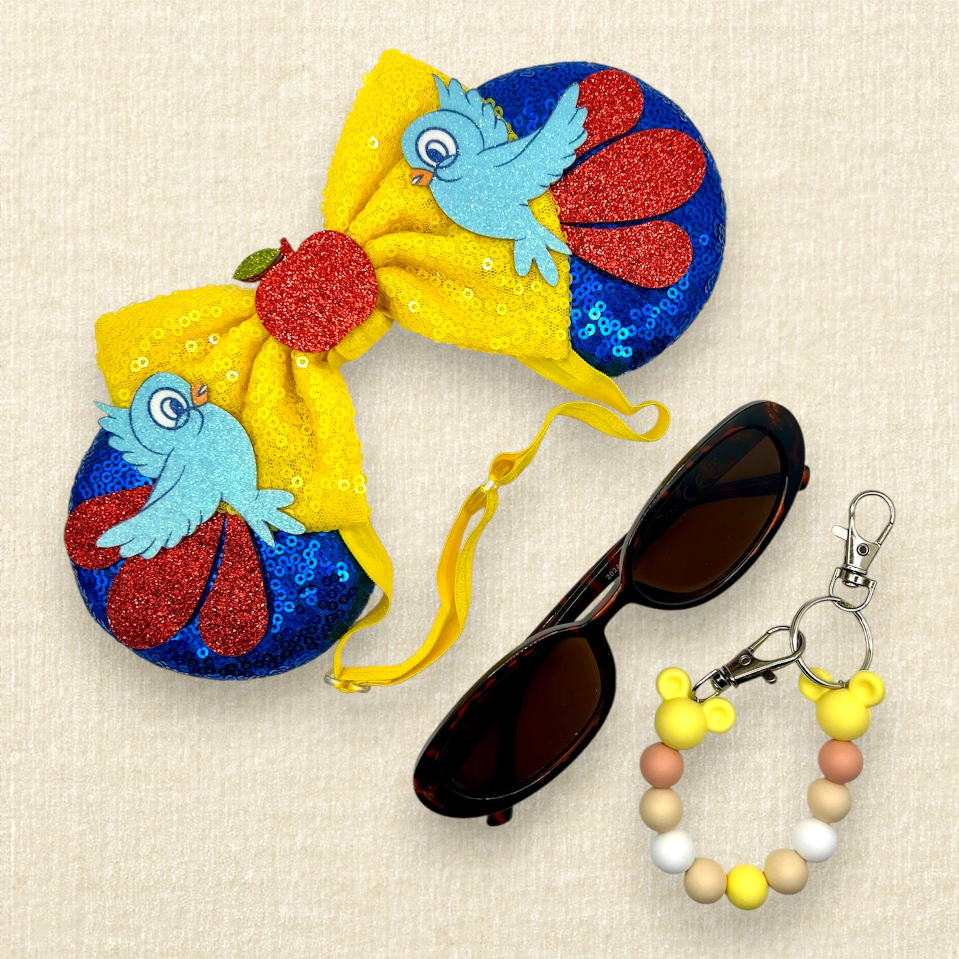 Blue sequin mouse ears with yellow bow, red glitter details, glitter bluebirds, and a red glitter apple centerpiece; sunglasses; beaded mouse ears holder