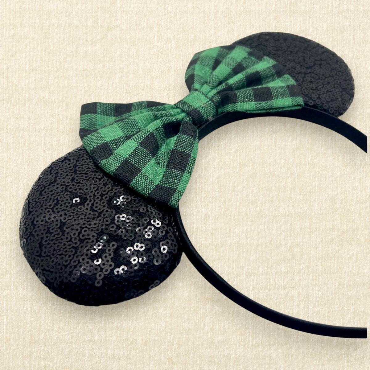 A festive Christmas-themed mouse ears headband with black sequin ears and a green and black buffalo plaid bow.