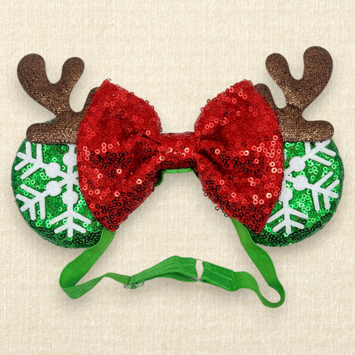 Christmas themed mouse ears headband with green sequin ears, white snowflake details, red sequin bow, and brown glitter reindeer antlers on an elastic headband