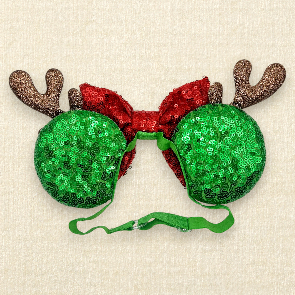 Christmas themed mouse ears headband with green sequin ears, white snowflake details, red sequin bow, and brown glitter reindeer antlers on an elastic headband (back view)