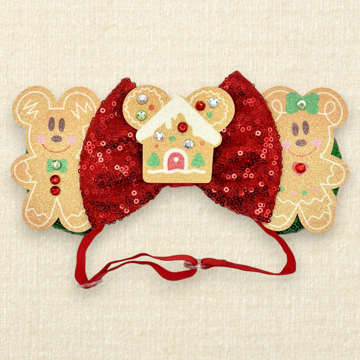 A festive Christmas mouse ears headband featuring two gingerbread mouse cookies, a red sequin bow, and a gingerbread house in the center, with a red elastic headband.