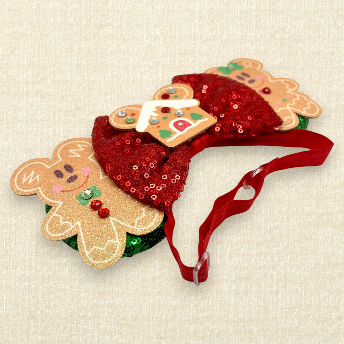 A festive Christmas mouse ears headband featuring two gingerbread mouse cookies, a red sequin bow, and a gingerbread house in the center, with a red elastic headband.