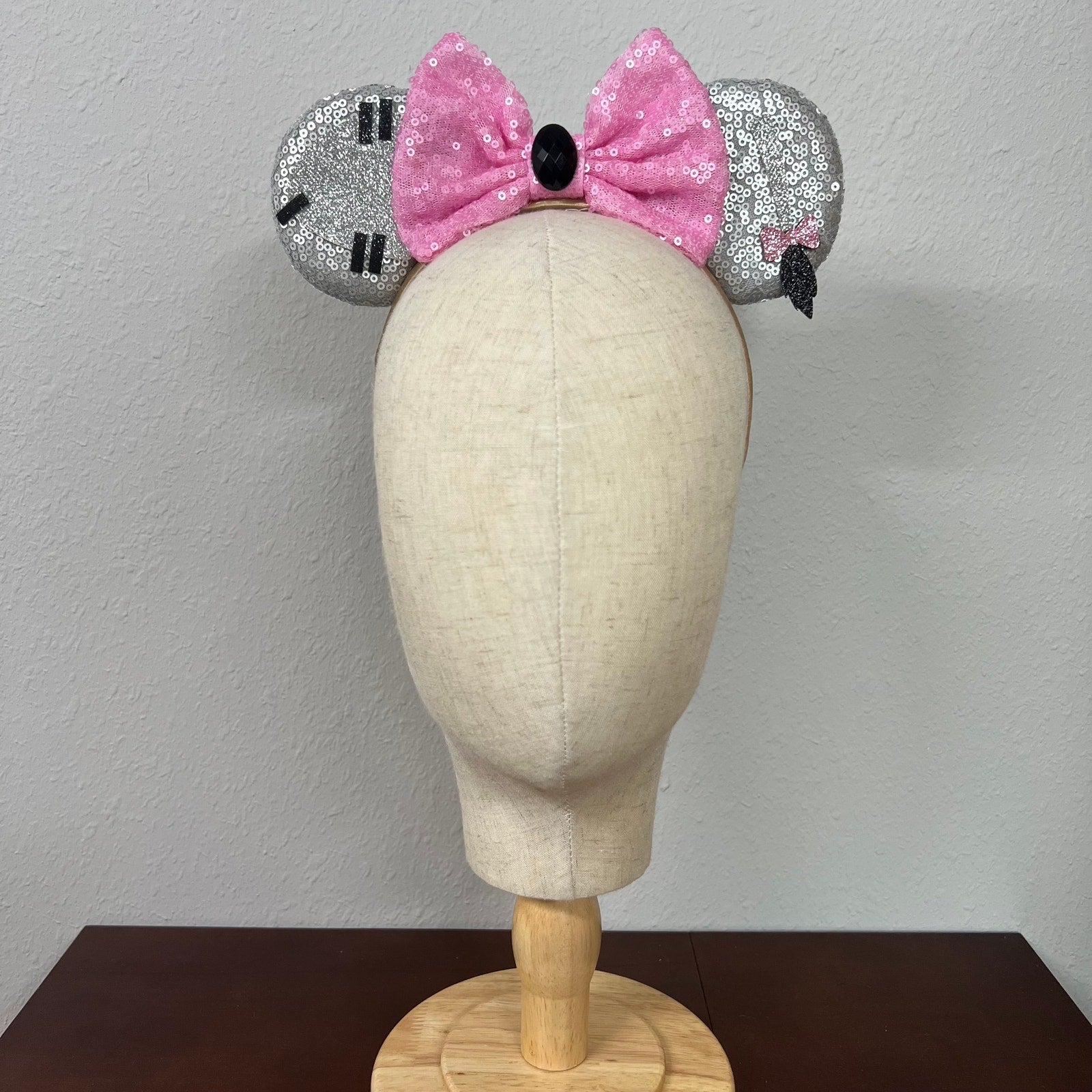 Mannequin head wearing silver and pink sequin mouse ears against a plain background