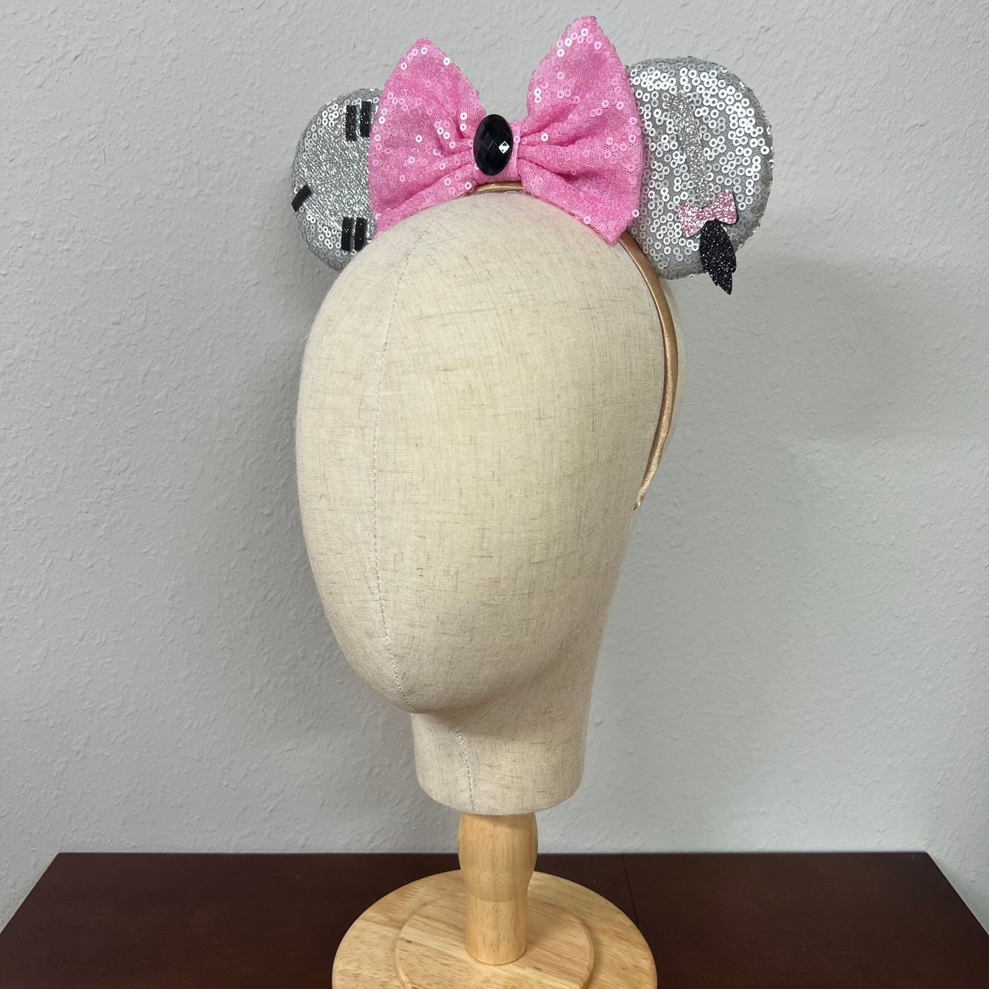 Mannequin head wearing silver and pink sequin mouse ears against a plain background