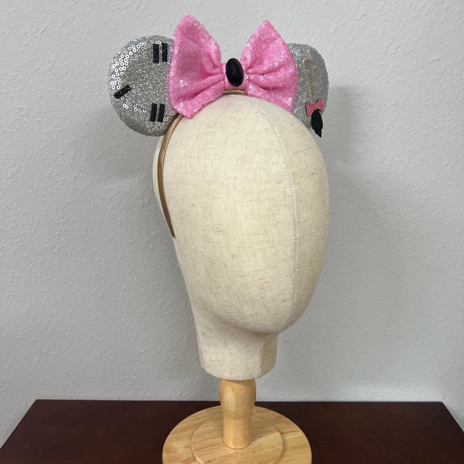 Mannequin head wearing silver and pink sequin mouse ears against a plain background