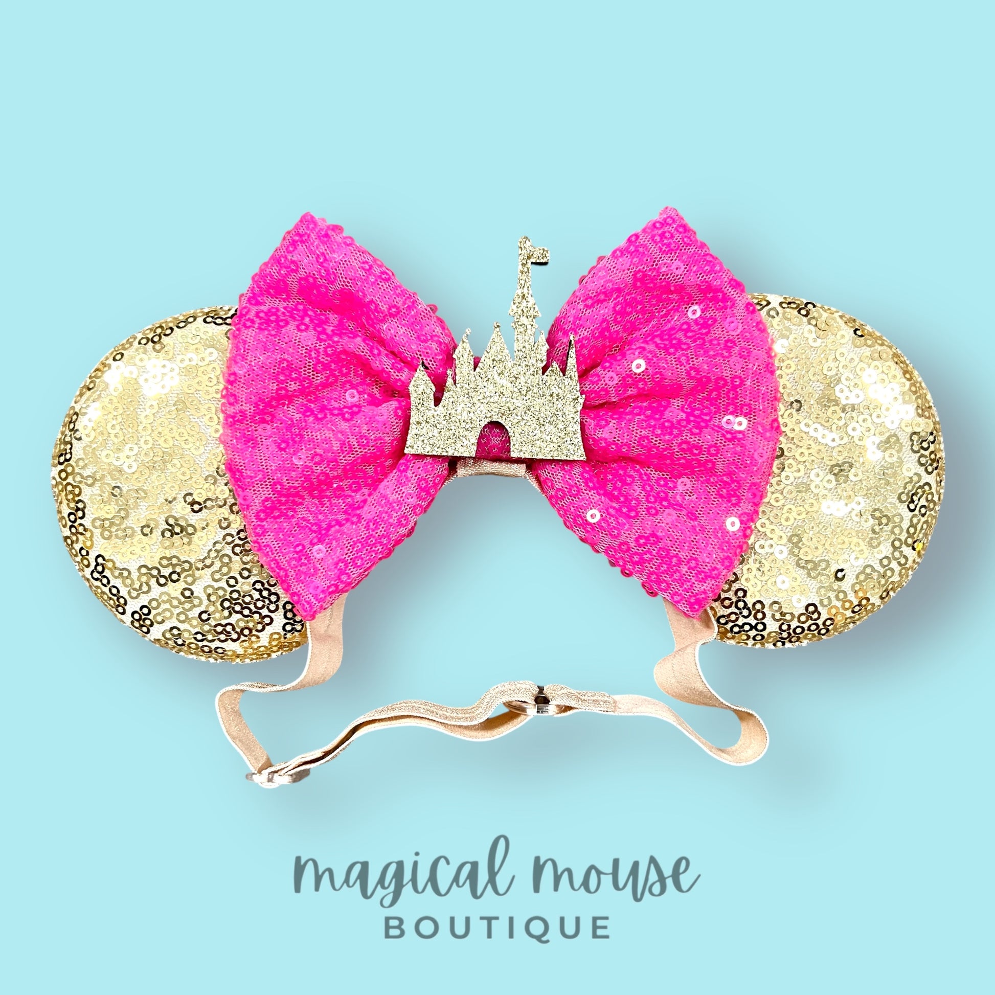 Gold and pink mouse ears with a castle design on a light blue background