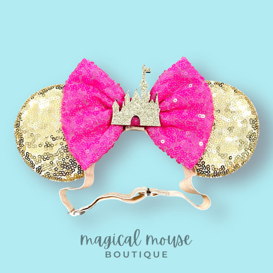 Gold and pink mouse ears with a castle design on a light blue background