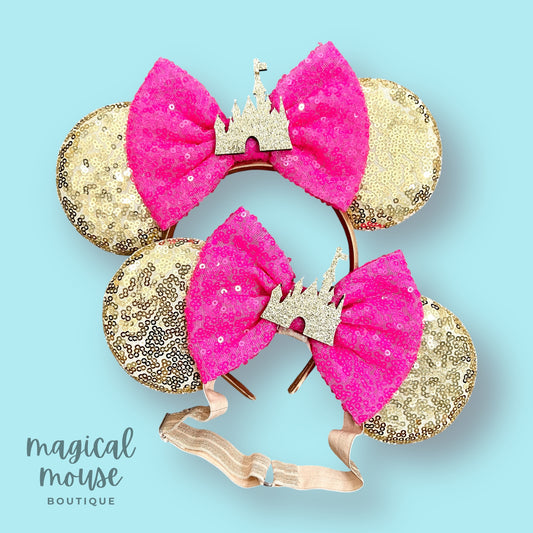 Gold and pink Mommy & Me mouse ears set with gold castles on a light blue background