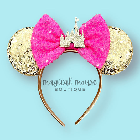 Pink and gold mouse ears with a castle design on a light blue background