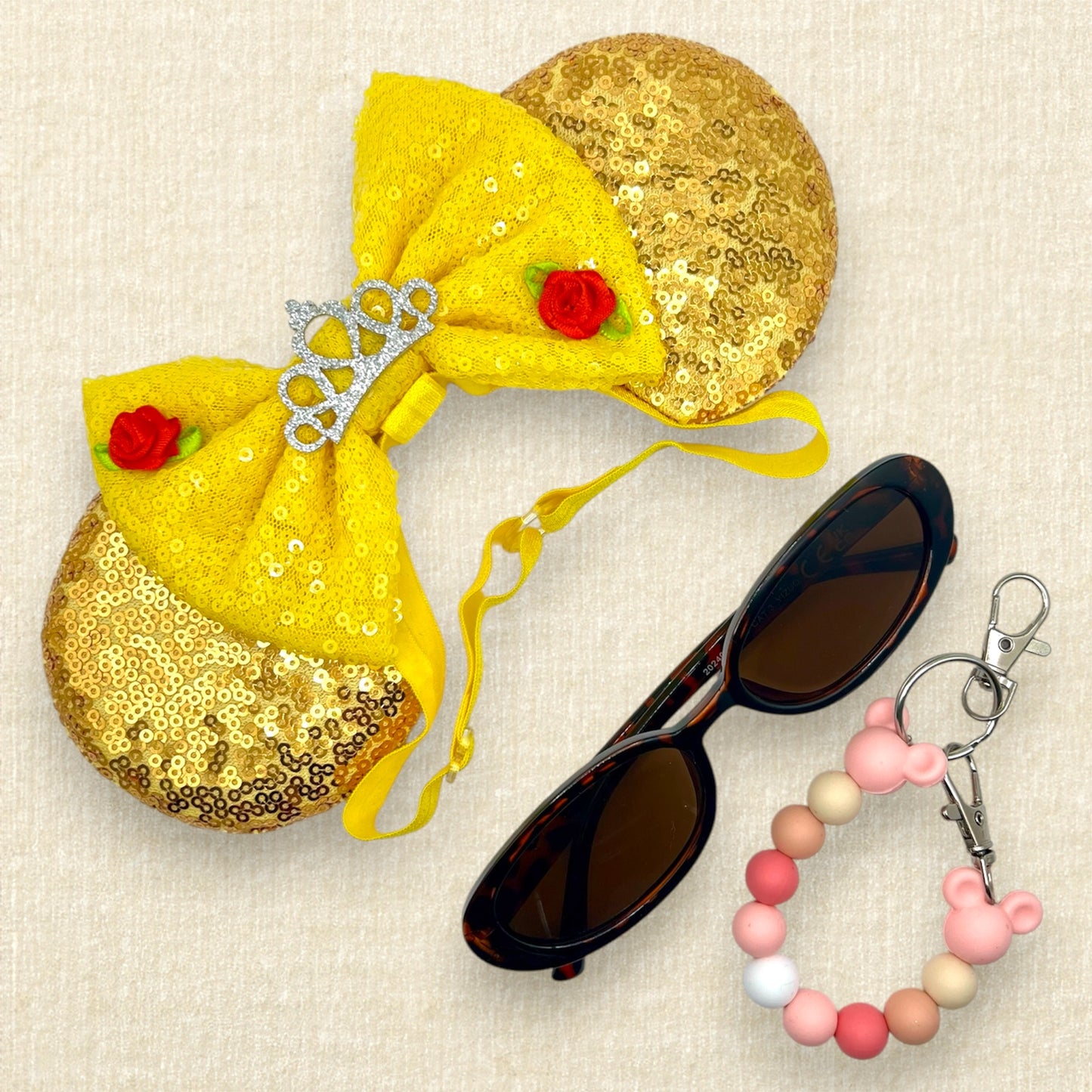 Gold sequin mouse ears with a yellow bow, silver tiara, and red roses on an elastic headband; sunglasses; pink beaded mouse ears holder keychain