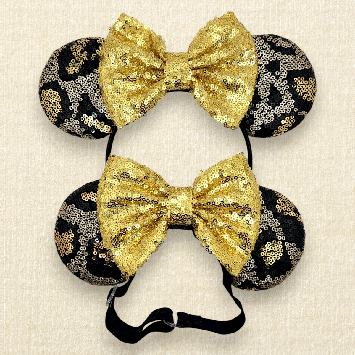 Two pairs of matching black and gold sequin animal print mouse ears with gold sequin bows - one with a standard headband and the other with an elastic headband.