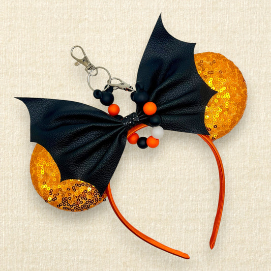 Halloween-themed mouse ears with orange sequin ears and black faux leather bat wing bow, with an orange and black beaded mouse ears holder keychain
