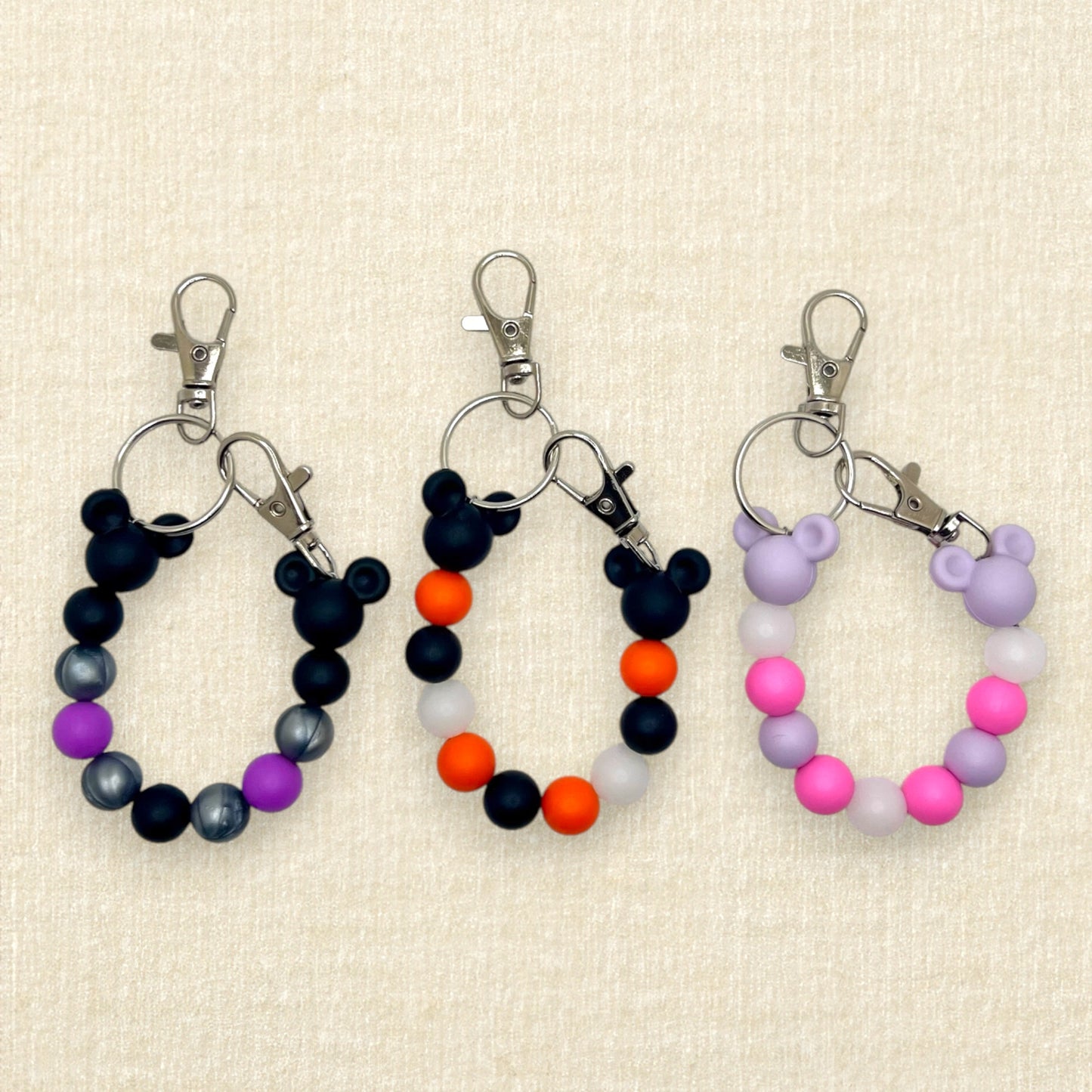 Three pairs of colorful beaded Halloween mouse ears holder keychains: purple, black, and silver; black and orange; lavender and pink