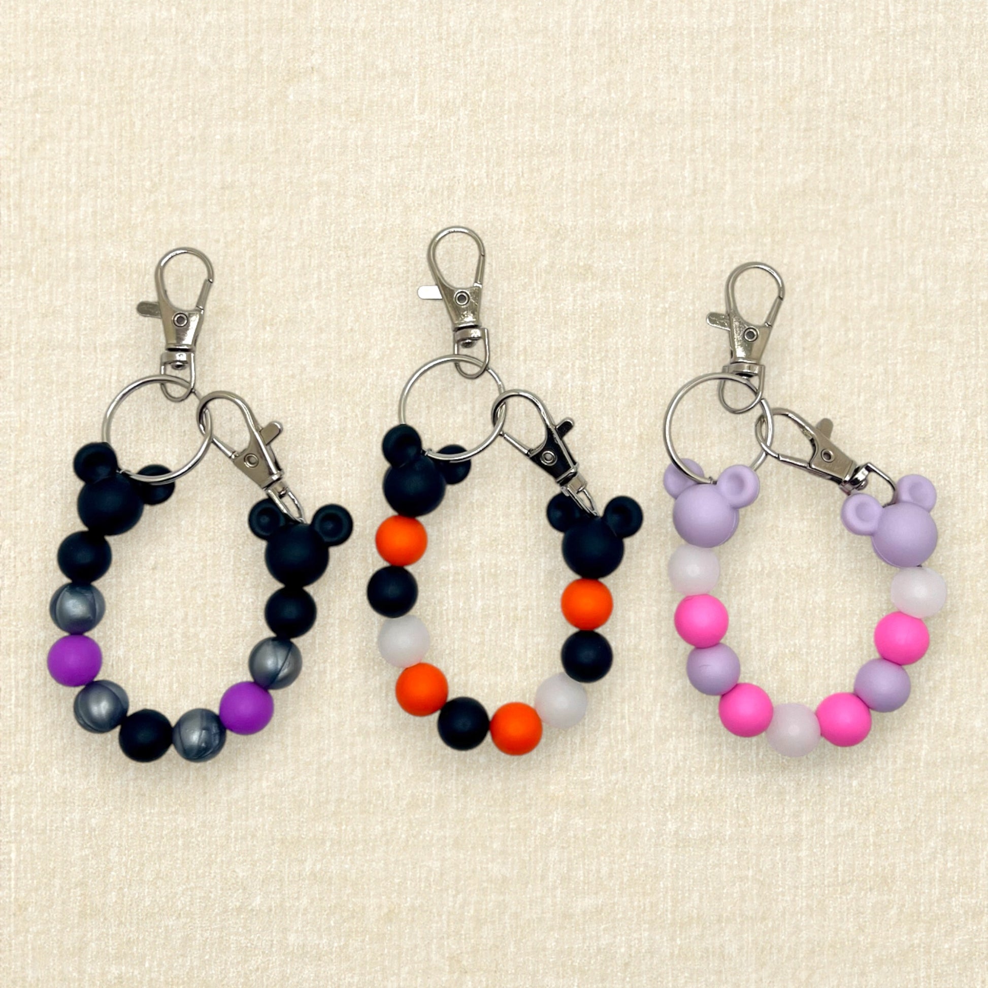 Three pairs of colorful beaded Halloween mouse ears holder keychains: purple, black, and silver; black and orange; lavender and pink