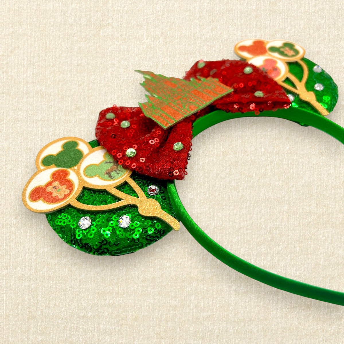 A Christmas-themed mouse ears headband with green sequin mouse ears, red sequin bow, and glitter red and green castle and holiday mouse balloon details.