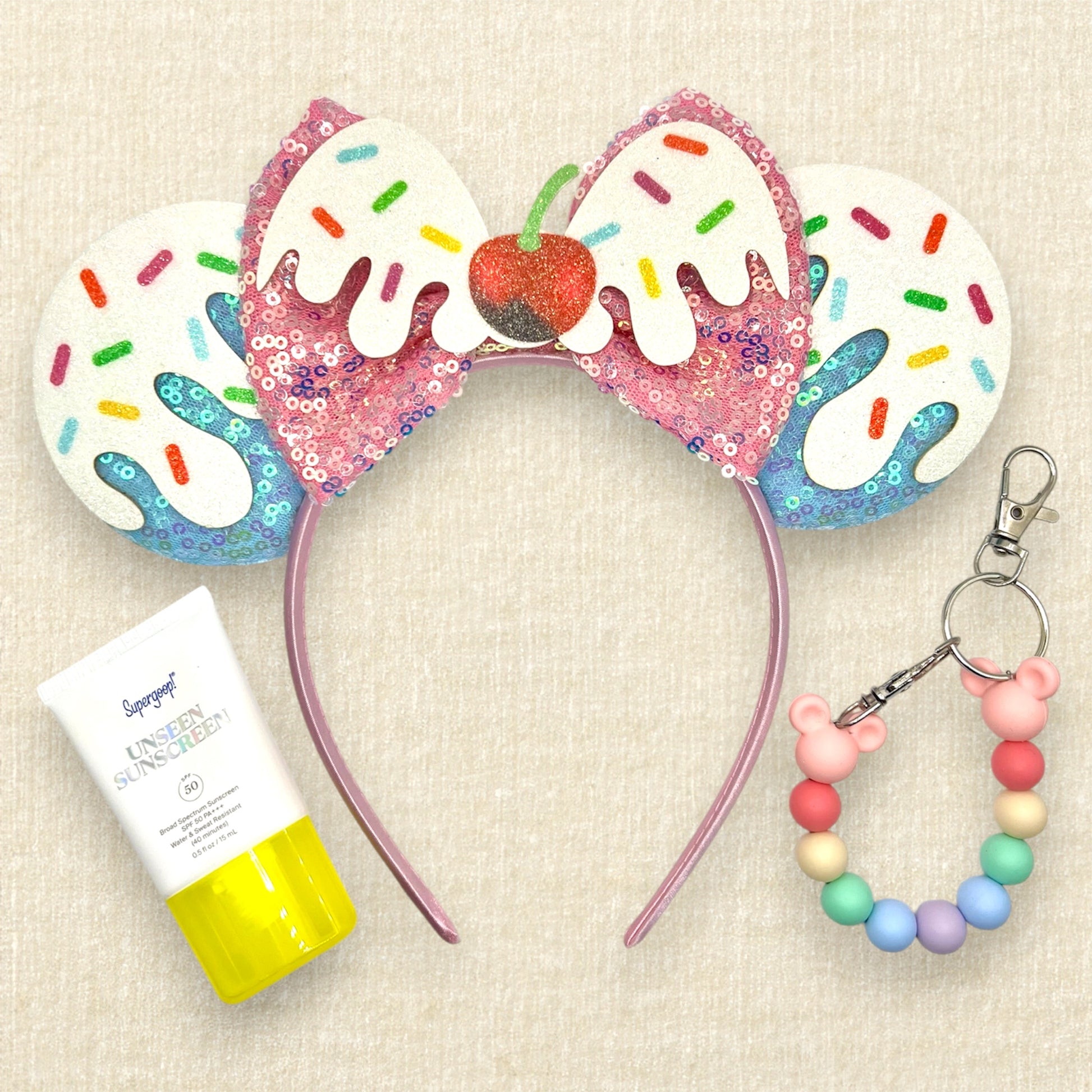 Colorful blue and pink ice cream-themed headband with sprinkles and cherry; small sunscreen; colorful beaded mouse ears holder