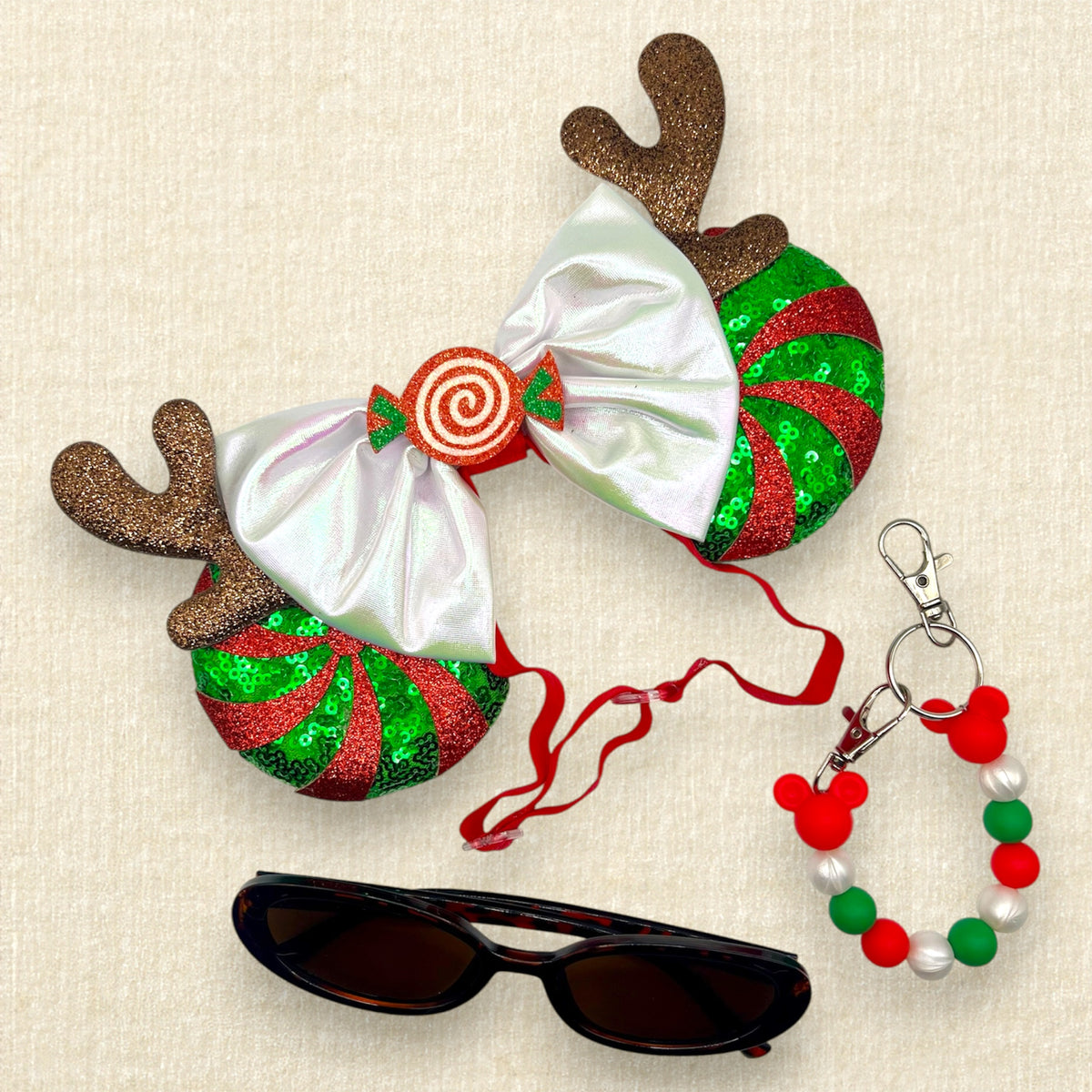Christmas-themed elastic mouse ears headband with glittery reindeer antlers, red and green peppermint candy cane swirl, an iridescent white bow, and a red spiral candy center; brown tortoiseshell sunglasses; red, pearl white, and green beaded mouse ears holder clip keychain