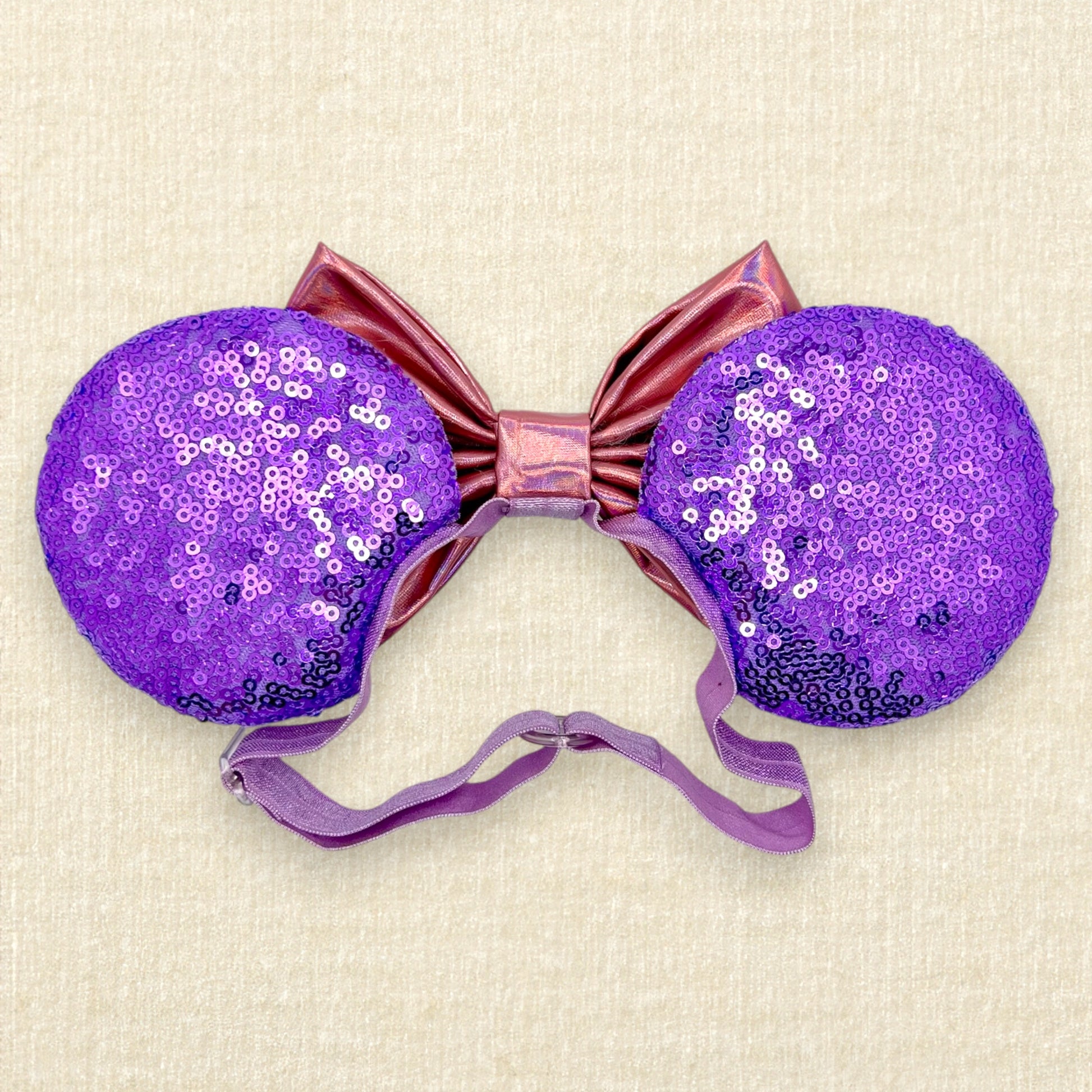 Halloween-themed mouse ears with purple sequin mouse ears, white glitter Mickey & Minnie ghosts, rhinestones, and an iridescent pink bow on an elastic headband (back view)