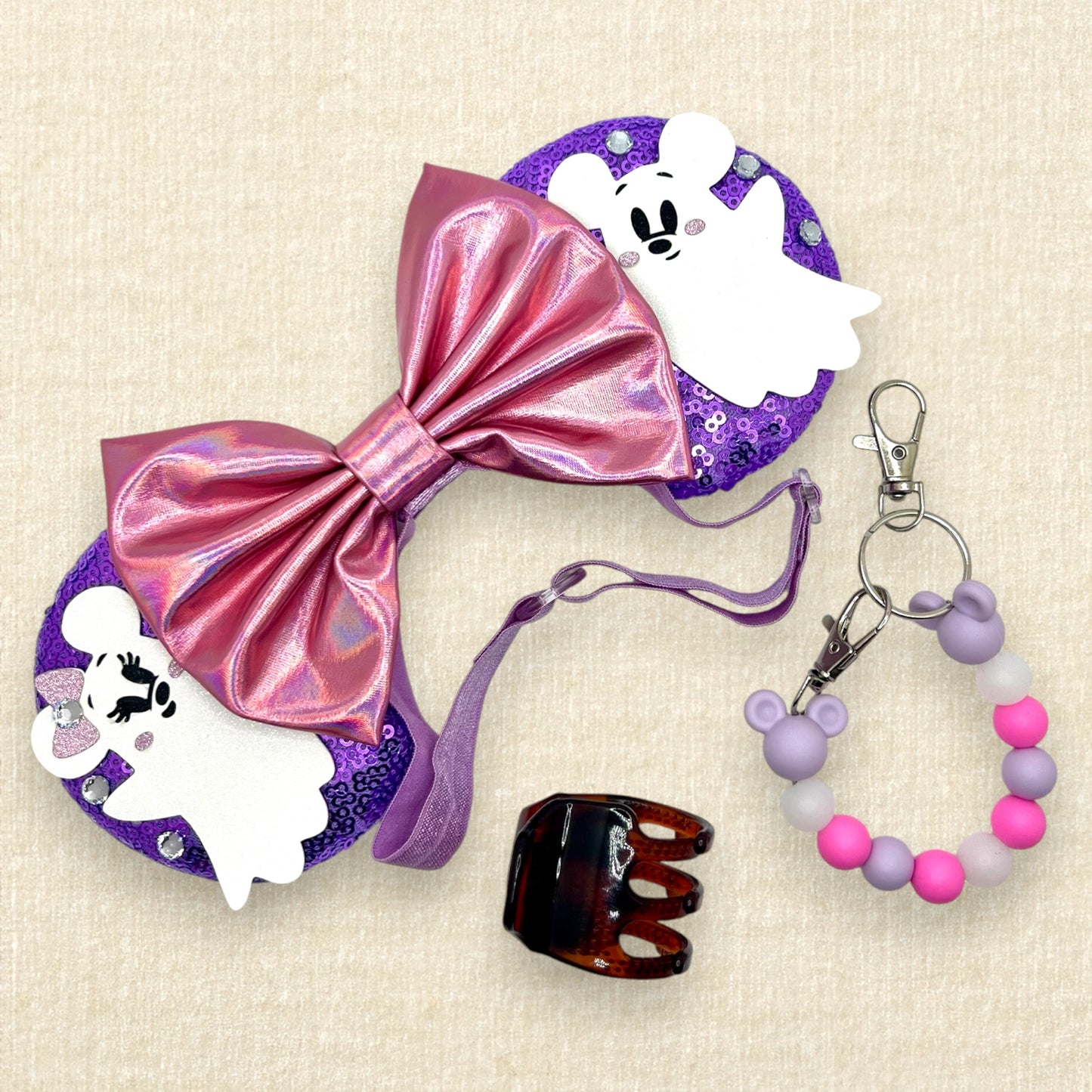 Halloween-themed mouse ears with purple sequin mouse ears, white glitter Mickey & Minnie ghosts, rhinestones, and an iridescent pink bow on an elastic headband; tortoiseshell claw clip; pink and purple beaded mouse ears holder keychain
