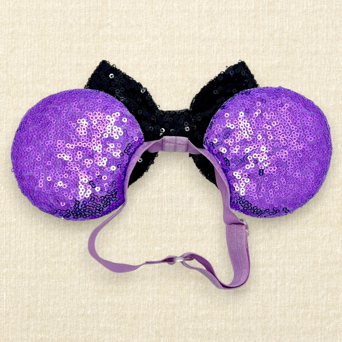 Halloween-themed mouse ears with purple sequin mouse ears, glitter Mickey and Minnie pumpkins, black sequin bow, and rhinestones on an elastic headband (back view)