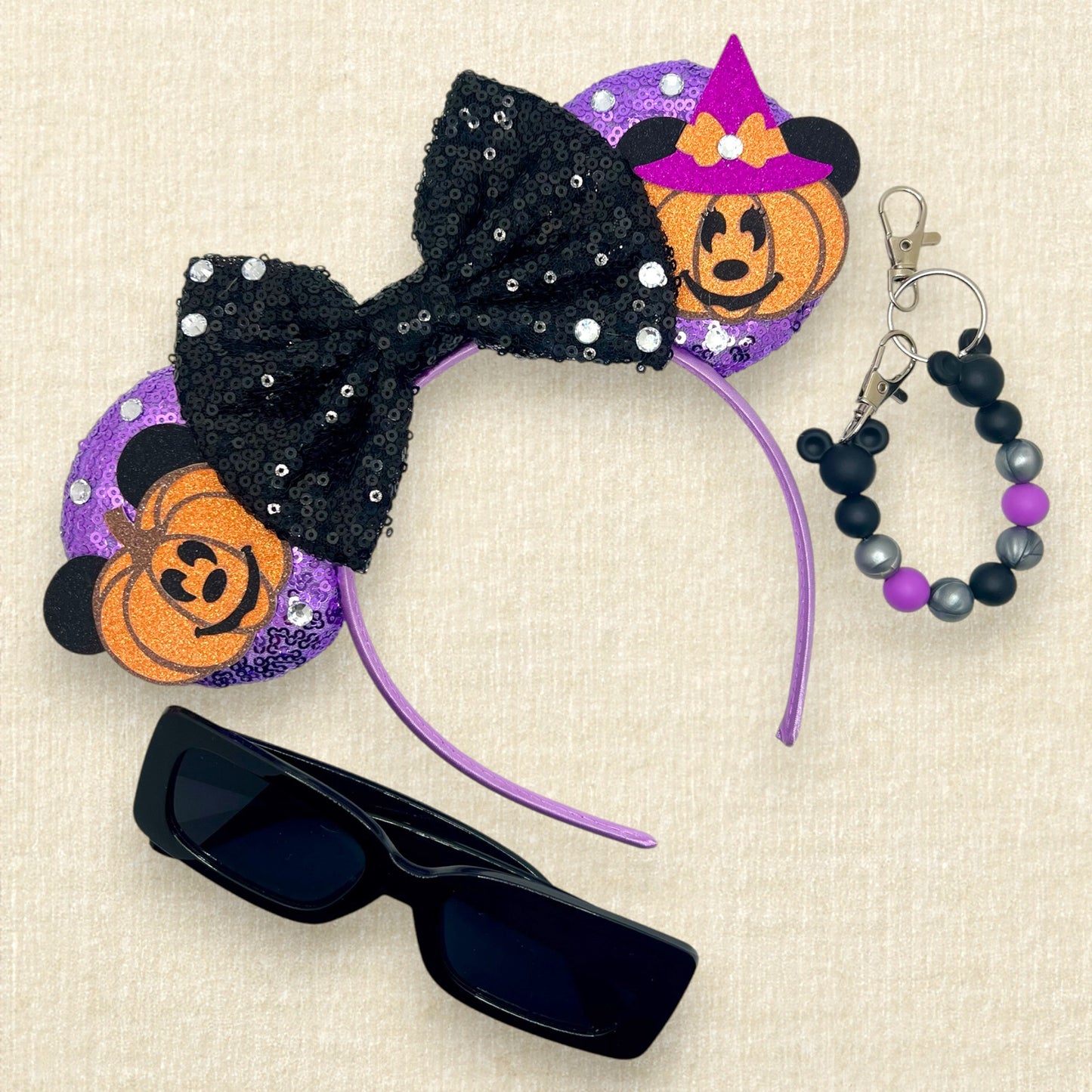 Purple sequin mouse ears with pumpkin Mickey and Minnie and black sequin bow; black sunglasses; purple, black, and silver beaded mouse ears holder keychain