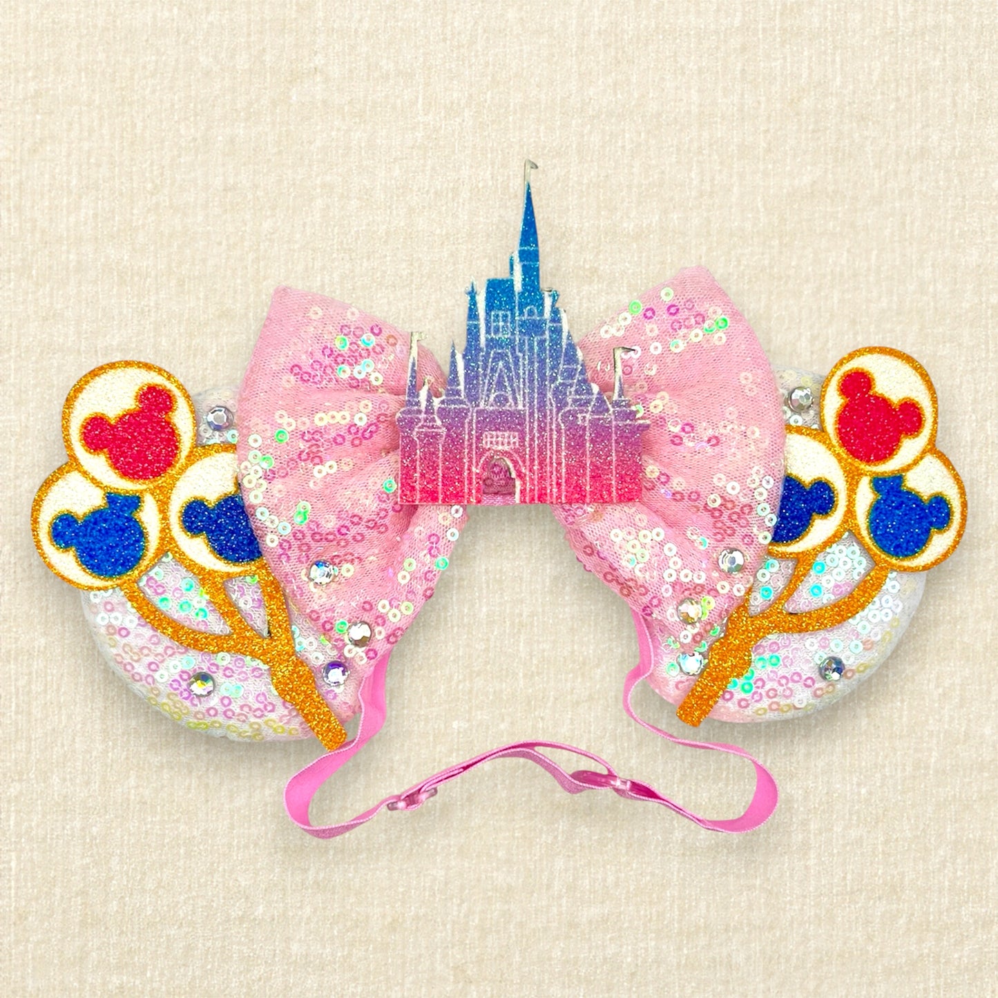 White sequin mouse ears with colorful mouse balloons and a pink bow with pastel pink and blue castle centerpiece on an elastic headband