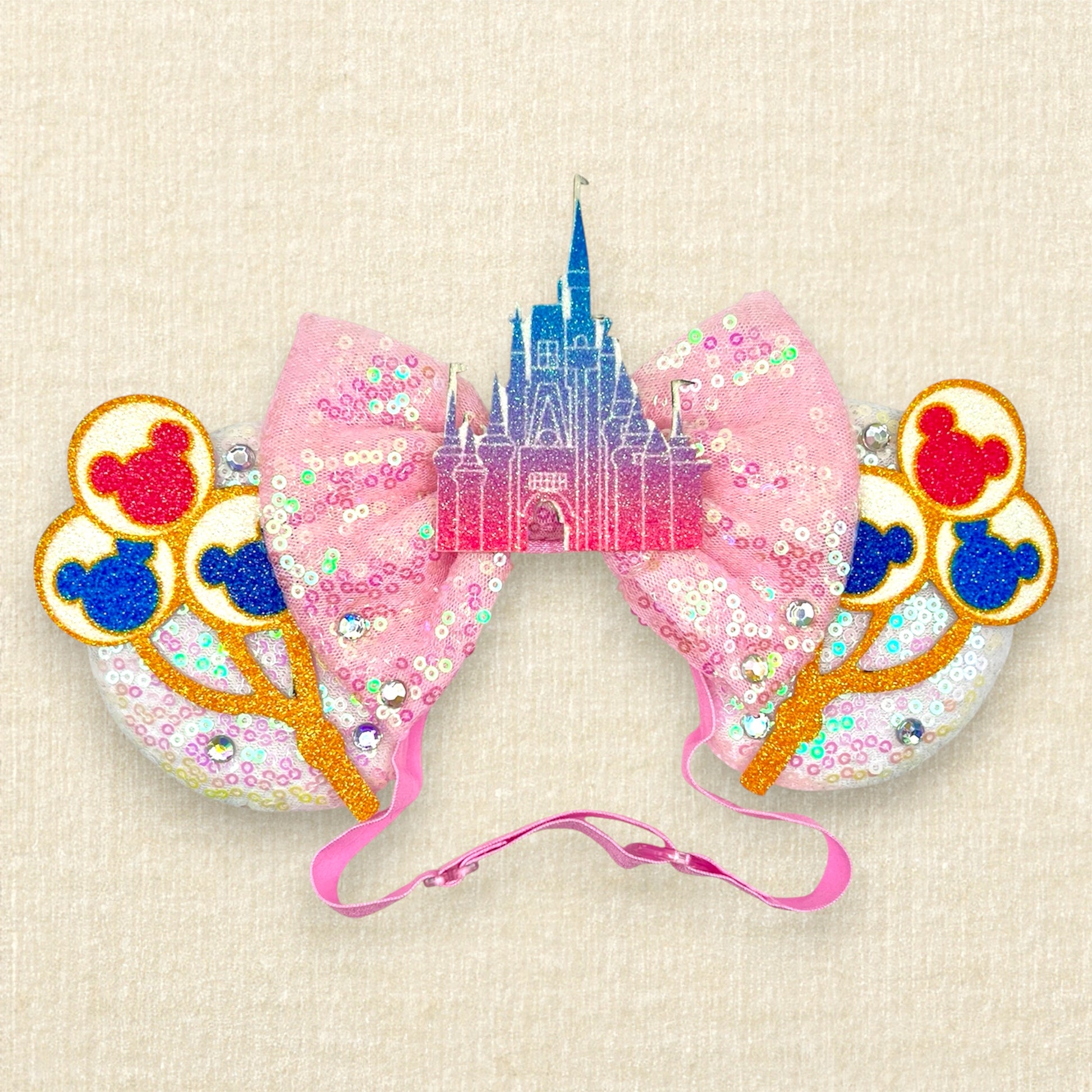 White sequin mouse ears with colorful mouse balloons and a pink bow with pastel pink and blue castle centerpiece on an elastic headband